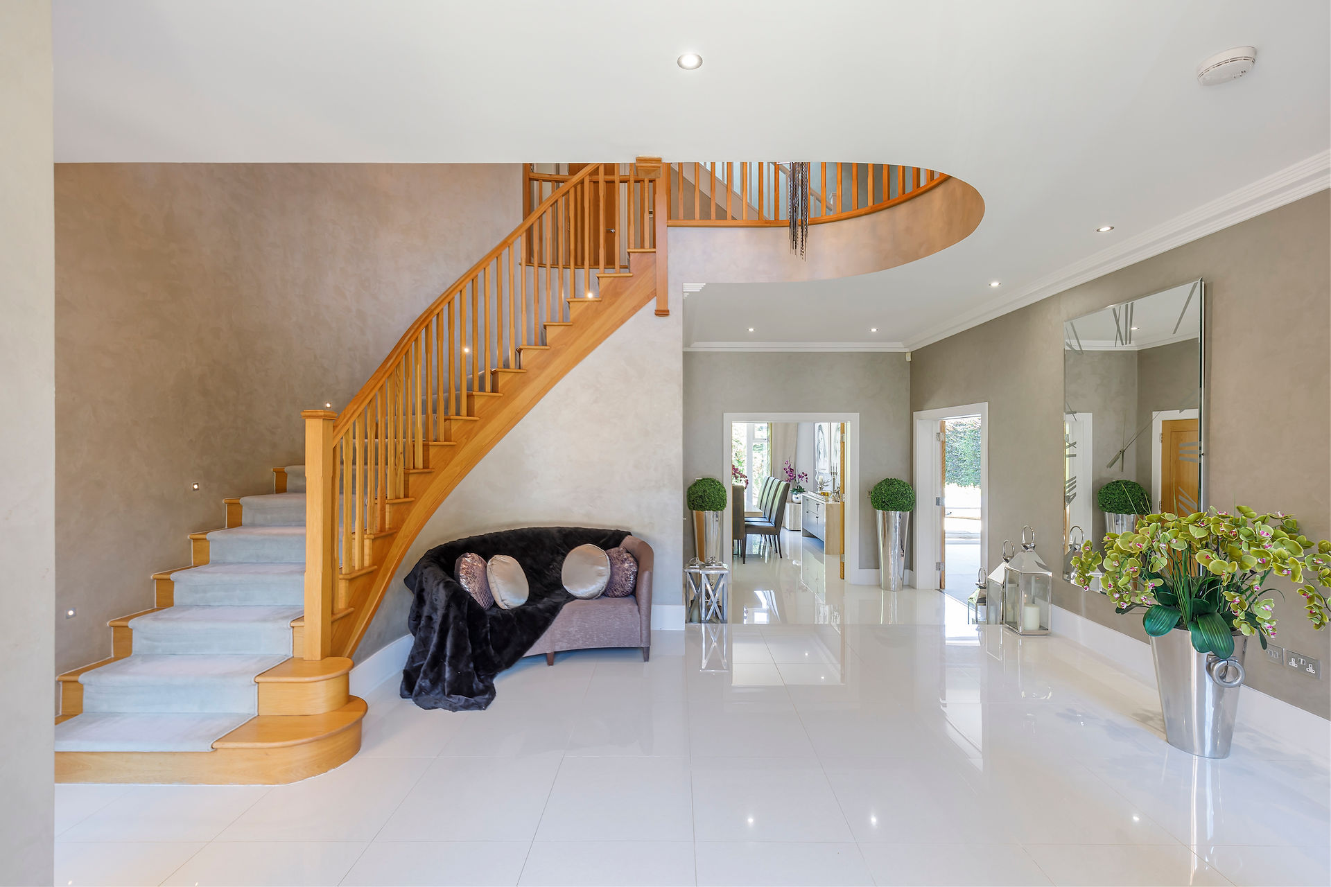 Luxury entrance hall with curved wooden staircase, polished floor and high ceiling in a UK family home
