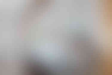 Rustic cottage bedroom with exposed ceiling beams, wooden bed frame, neutral bedding, and small window overlooking greenery