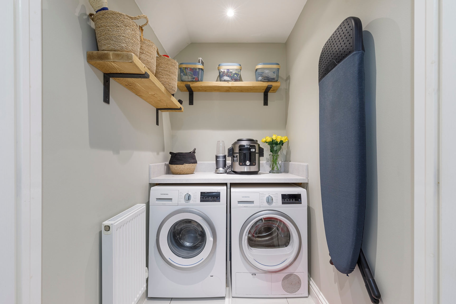 Compact utility room with washing machine, tumble dryer, wooden shelves and ironing board