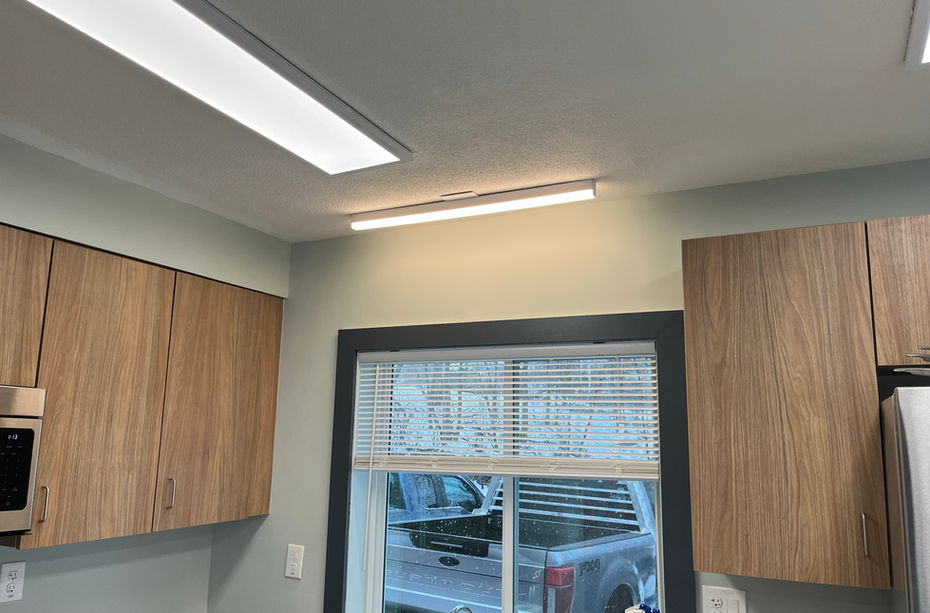Modern kitchen cabinets, window with blinds, and bright overhead LED lighting.