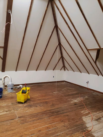 Unfinished attic room with exposed wooden beams, wood floor, and equipment.