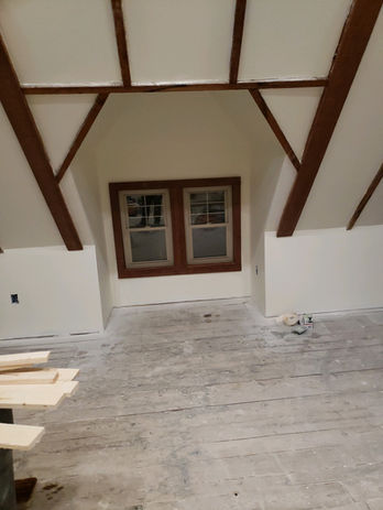 Unfinished attic room with exposed wooden beams, double window, and rough floor.