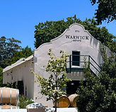 Weißes kapholländisches Weingutsgebäude von Warwick mit Holzfässern in Stellenbosch.