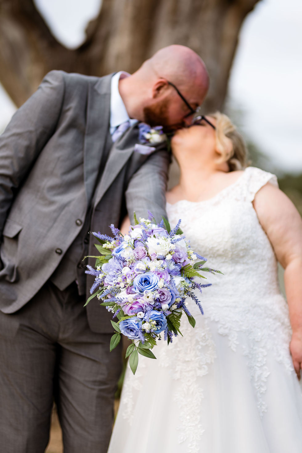 a bride and groom kissing while the bride holds a bouquet of blue and white flowers