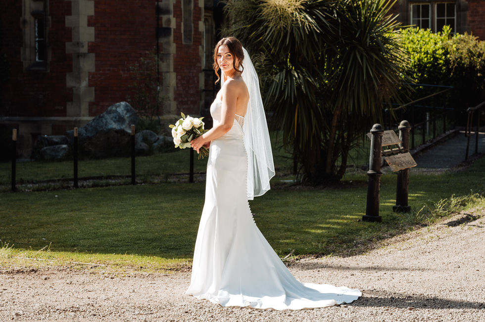Bride in white dress holding bouquet outdoors.
