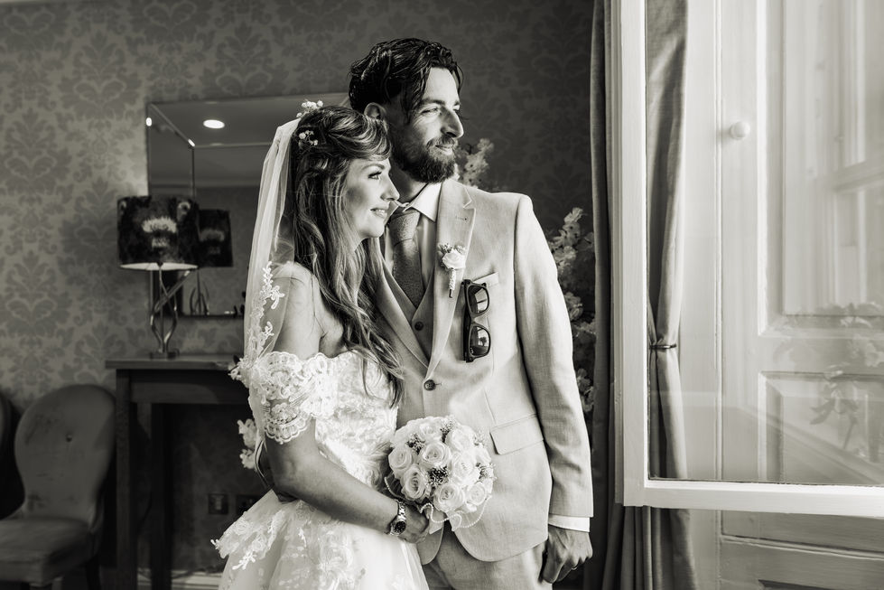 Bride and groom standing by a window, smiling.