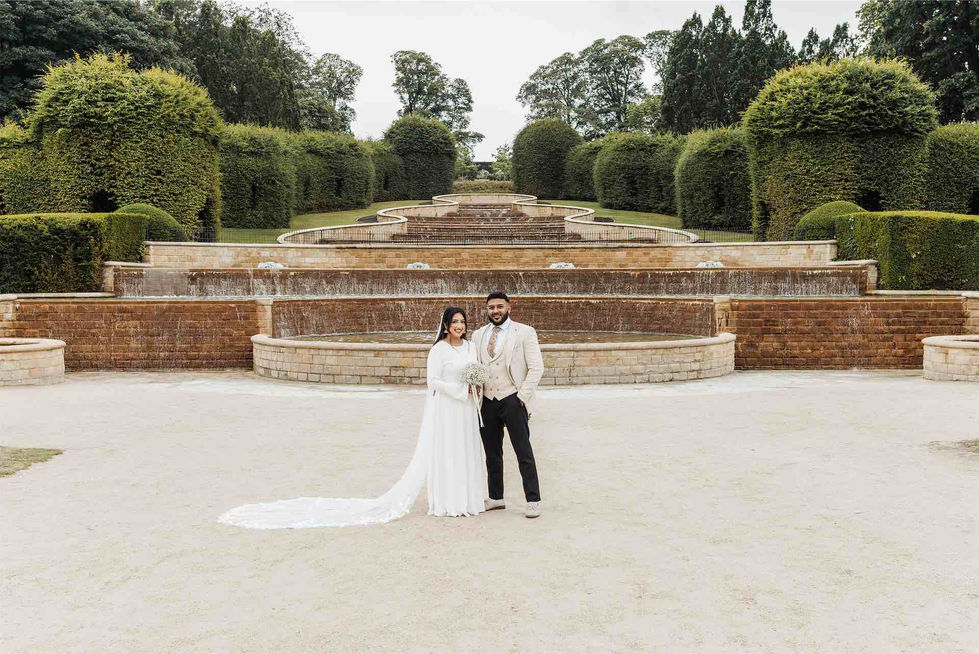 Couple posing in front of tiered garden fountain.