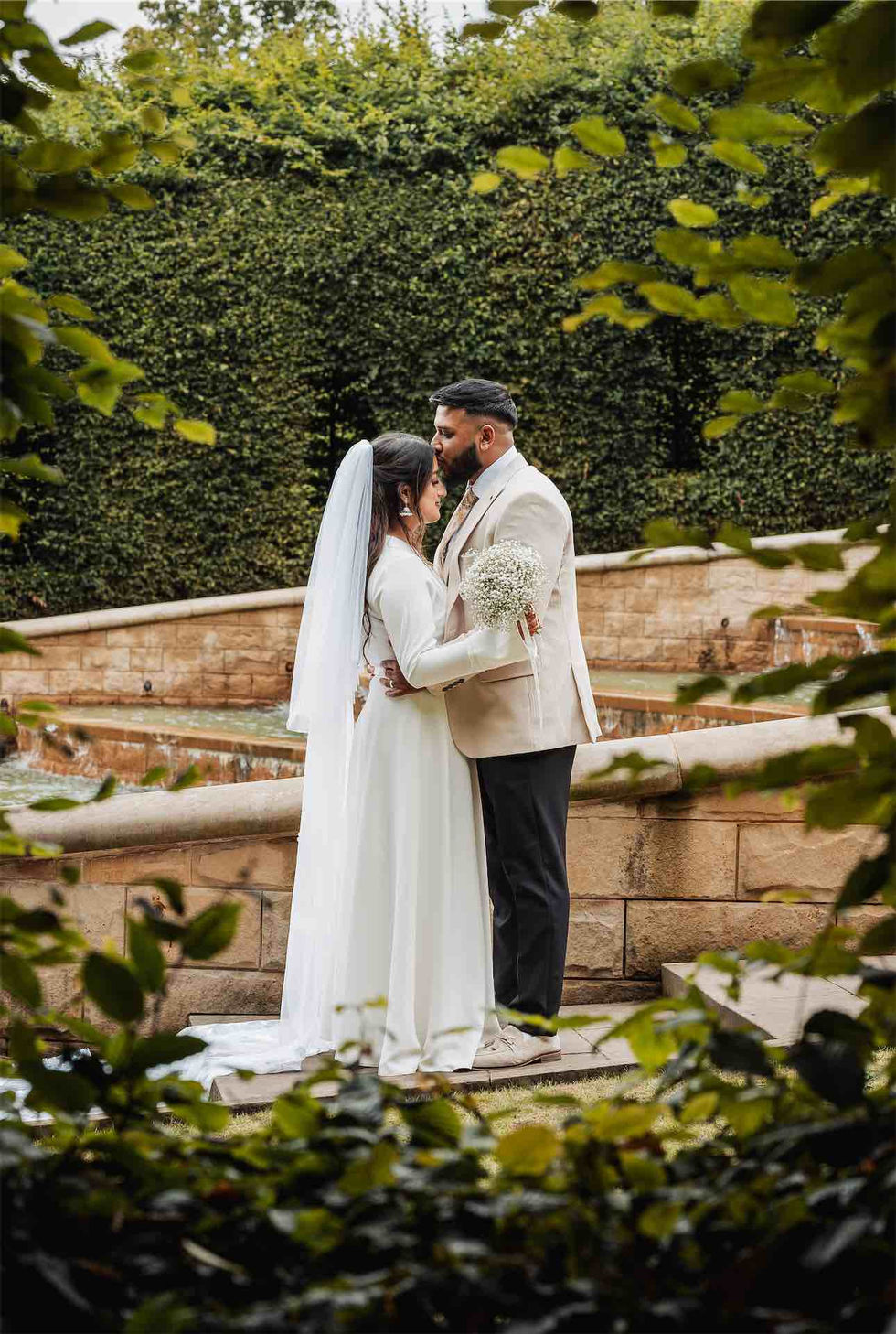 Bride and groom embracing in garden setting.