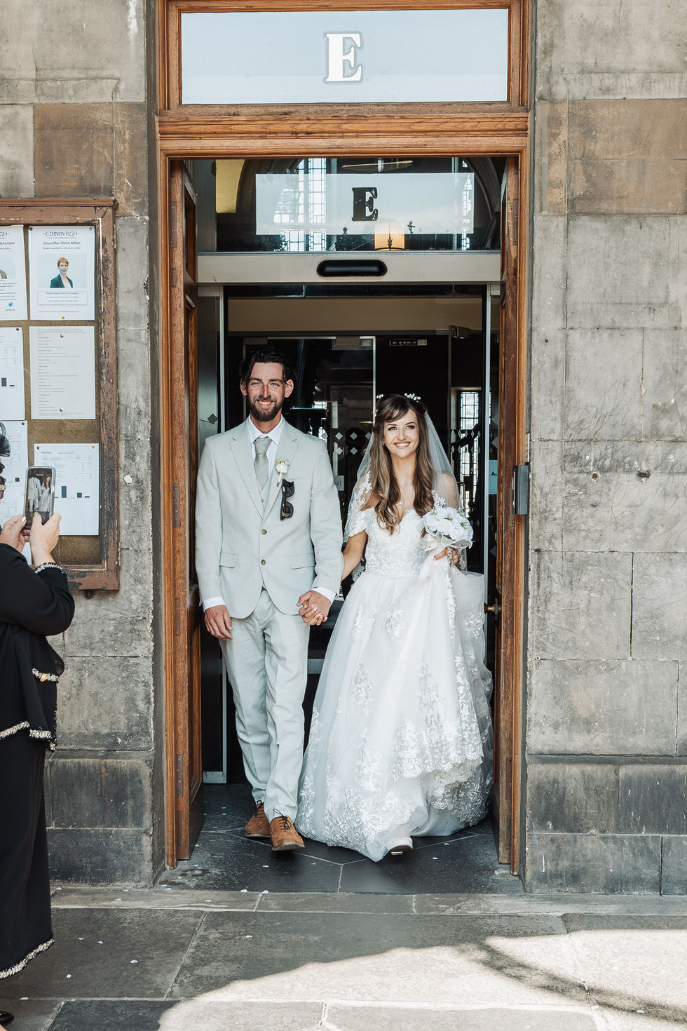 Bride and groom exiting a building, holding hands.