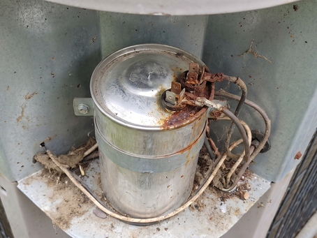 A rusted and bulging AC run capacitor inside an outdoor condenser electrical box showing thermal degradation.
