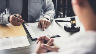 Business attorney in suit pointing to contract document while meeting with client across desk, gavel visible on table