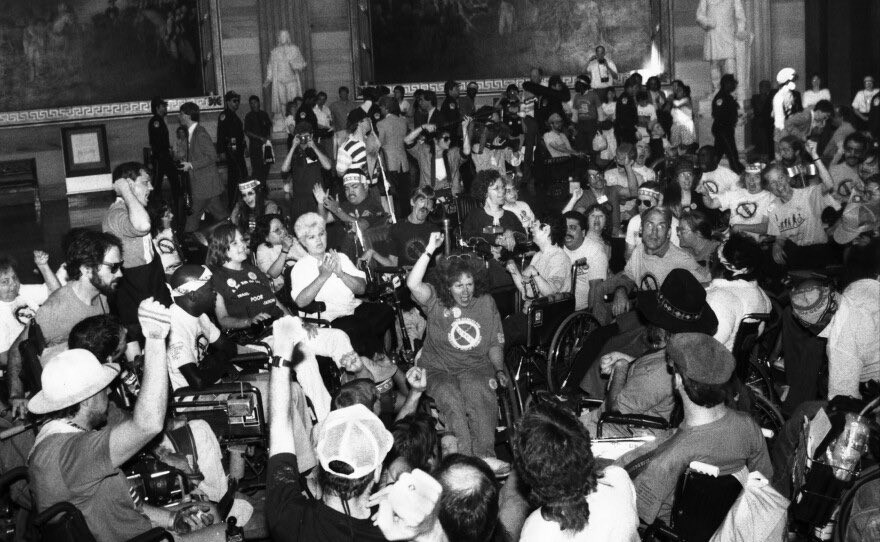 a room full of lively activists in wheelchairs protesting in a government building during the 504 Sit in