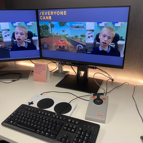 a screen showing a boy playing a video game. in front of the desktop screen is a pair of headphones