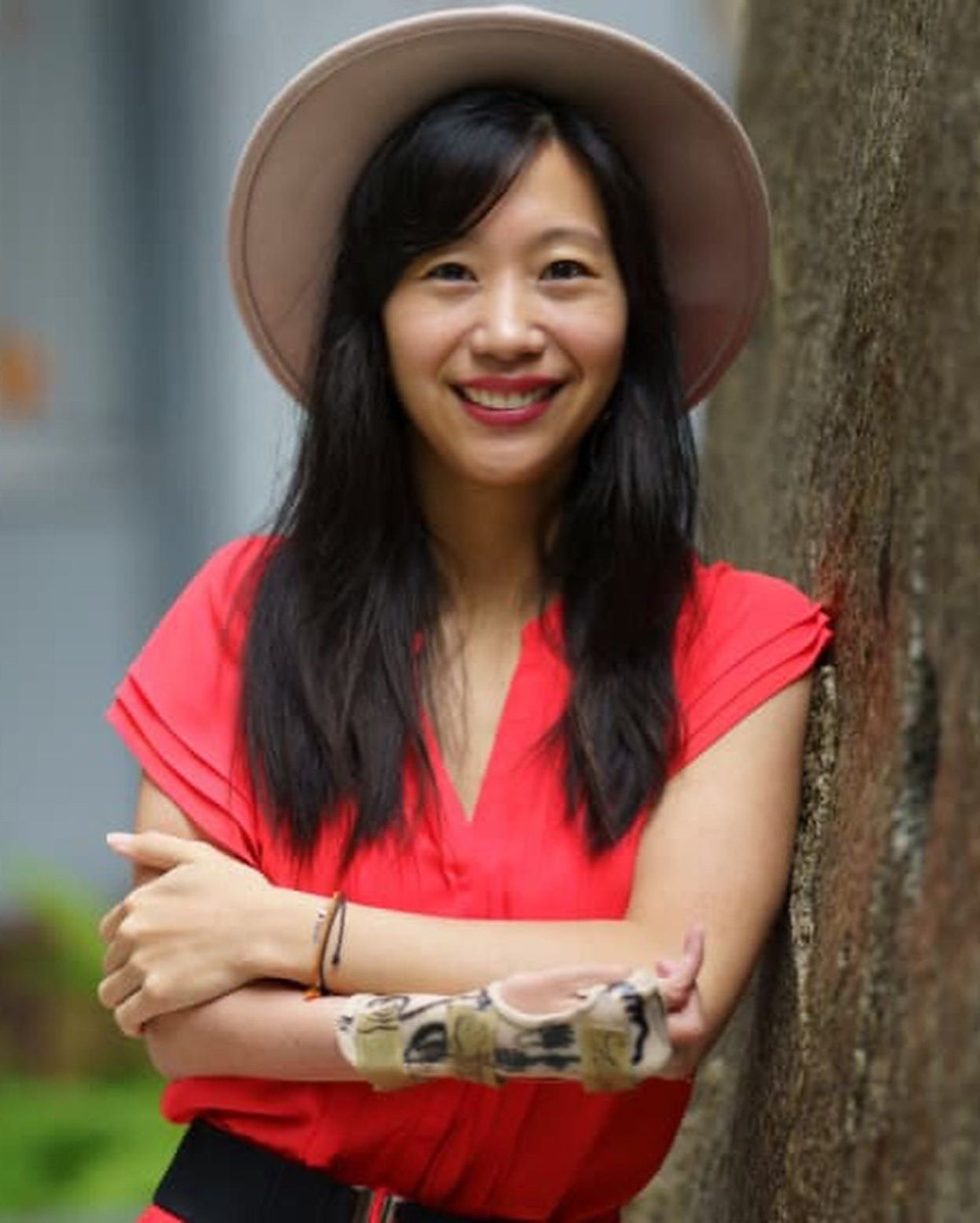 a young asian woman smiling at the camera with long brown hair and a wide brimmed hat. She has a hand brace