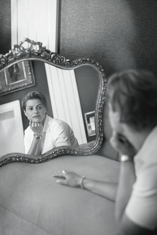 Eine Person schaut nachdenklich in einen verzierten Spiegel. Die Umgebung ist elegant und schlicht. Schwarz-Weiß-Foto mit ruhigem Ausdruck.