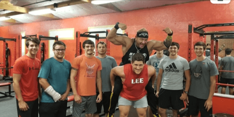 Omegaman flexes with high school athletes in a gym, promoting strength and leadership beyond the school assembly stage.