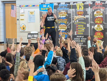 Omegaman speaks to an engaged group of students raising their hands during a school assembly about making good choices.