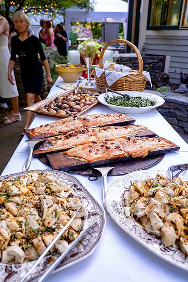 a buffet table featuring cedar planked salmon, potatoes, green beans, salads, a bread basket, and flowers