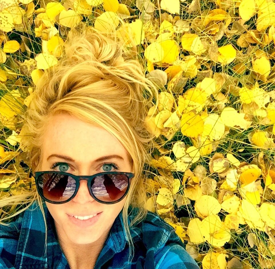 Sarah Reinen smiling in sunglasses, surrounded by yellow flowers