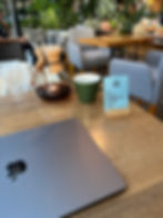 MacBook laptop on a wooden table in a cafe. A Chevex coffee cup can be seen in the background.