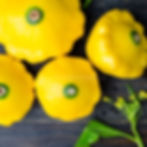 Sunburst F1 summer squash in a wooden box, on a table, and for sale at a market.