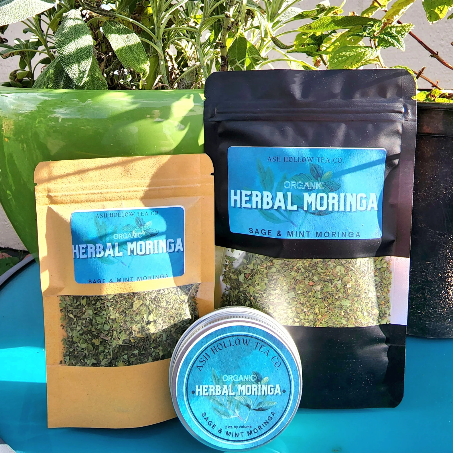 Two bags of Herbal Moringa tea made with moringa, spearmint, mint, and sage on a blue table.