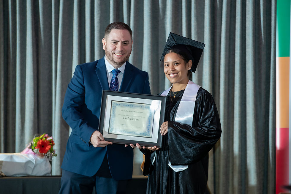 Michael Raymond (left) stands with Liz Vasquez (right) as they hold her scholarship. Liz is in a black cap and gown. Michael is in a blue suit.