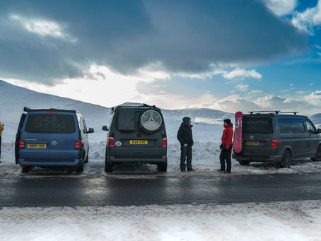 Three campervans parked up next to snowy mountain