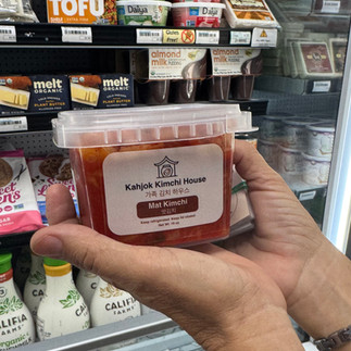 A hand holding a jar of Kahjok Kimchi House's mat kimchi at Village Foods & Pharmacy in Bryan, Texas