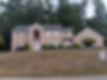 Large brick house with dark roof, trees, and sign in the front yard. Norm Weaver Roofing.