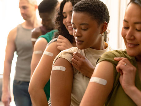 Group of people that just received vaccinations have their shirt sleeves rolled up and white bandages on their upper arms.
