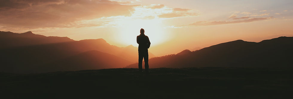 Silhouette of a person standing on a mountain ridge at sunset, with glowing orange sky and layered dark hills.