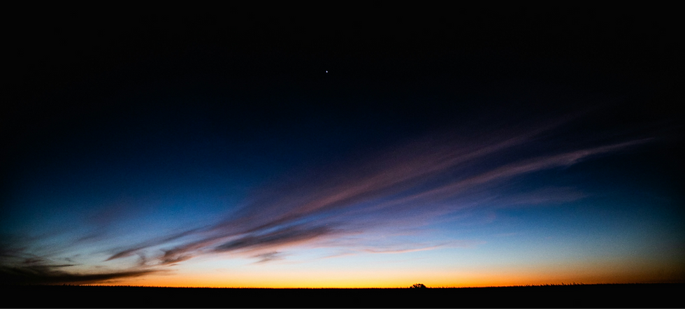 Dawn sky with a bright star above a dark horizon, streaked blue and purple clouds fading to orange at the horizon.