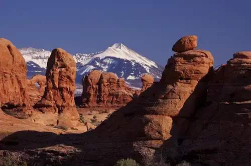 Red sandstone spires in a desert foreground with a snow-capped mountain and blue sky behind.