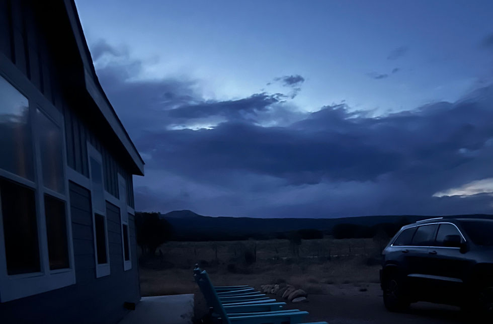 Dusk over a rural house and parked SUV, with a moody blue cloudy sky and dark hills in the background.