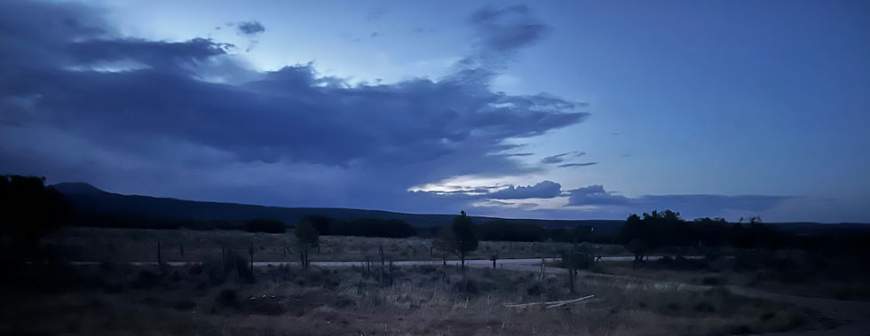 Blue dusk over a dark rural field with trees and a road, heavy clouds creating a calm, moody twilight scene