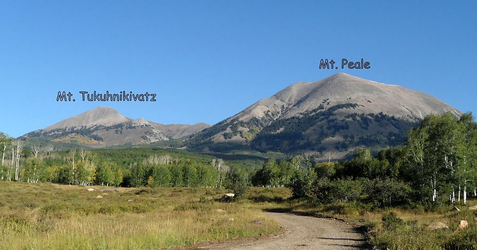 Mt. Tukuhnikivatz and Mt. Peale under a clear blue sky, with green forest and a dirt path in the foreground.