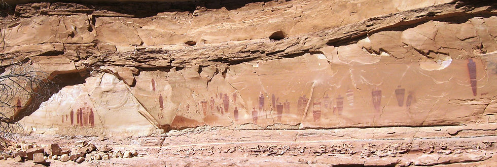 Sandstone canyon wall with faded ancient petroglyphs and rock art figures, sunlit desert scene with scattered rocks.