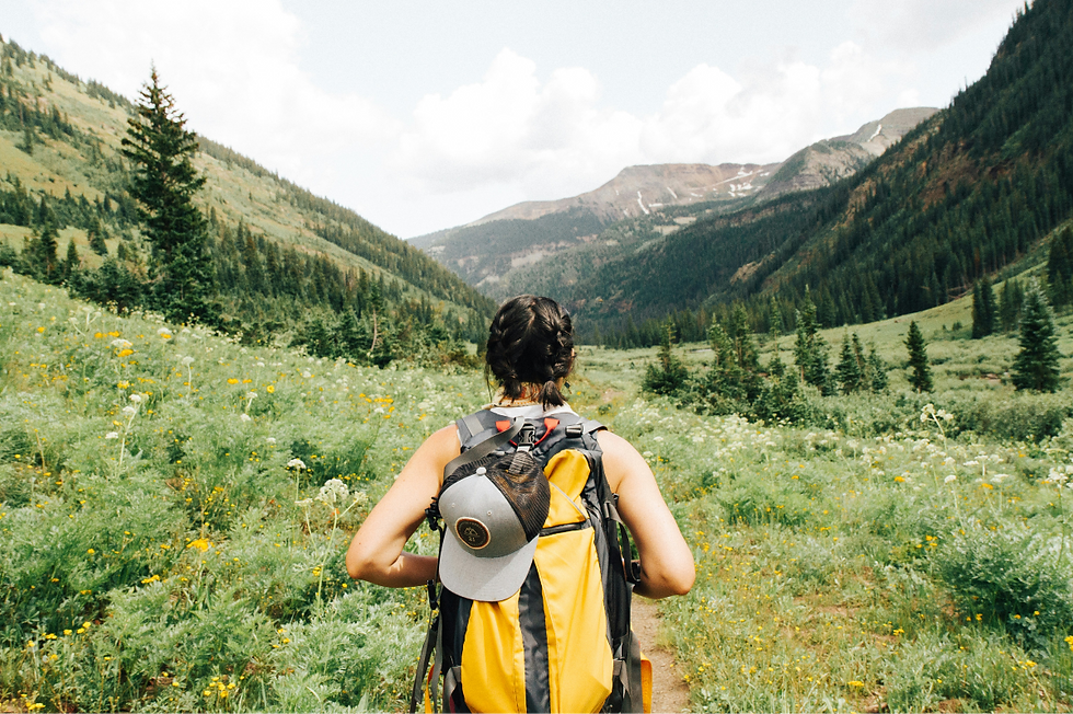 A hiker with a yellow backpack walks through a lush, green valley with mountains in the background under a cloudy sky. Embracing nature.