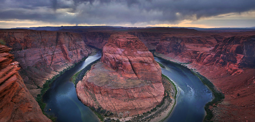 Horseshoe Bend canyon with a winding river around red sandstone cliffs under a dark, cloudy sky.