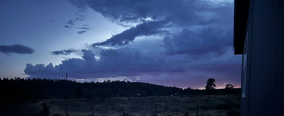 Dusk sky with dramatic blue-purple clouds over dark forest and field, with a building edge on the right.