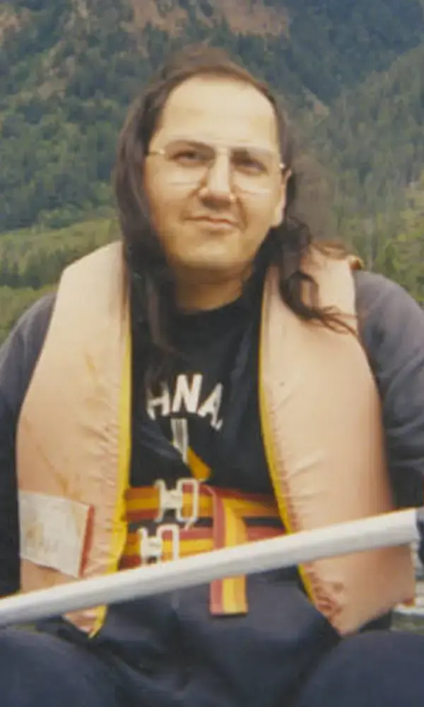 Photo of Albert McLeod in a life jacket, with an oar in a boat with mountains and forest behind
