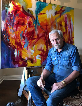 Robert Lombardi sitting in front of abstract painting with paintbrush in hand, The Lombardi Gallery, San Antonio Texas