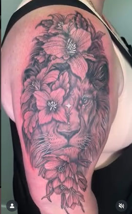 Black and grey lion tattoo with detailed lilies covering the shoulder and upper arm, designed by KarenM Tattoos