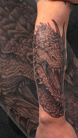 Black and grey dragon tattoo on the forearm with roaring expression and detailed scales.