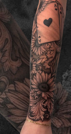 Tattoo of sunflowers and playing cards on the forearm, done in black and grey.