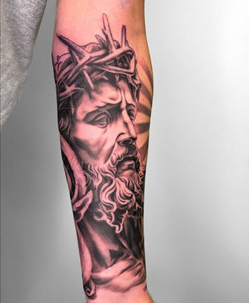 Black and grey tattoo of Jesus with crown of thorns on forearm, created by Jasmine Cabral, featuring realistic shading and religious symbolism.