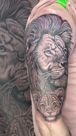 Lion and cub black and grey tattoo on the upper arm.