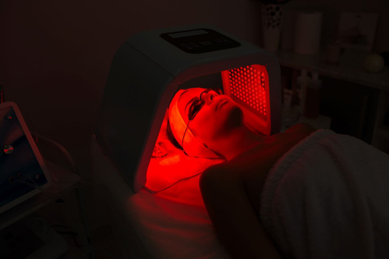 LED light therapy facial mask glowing blue and red, dark spa room, therapeutic atmosphere