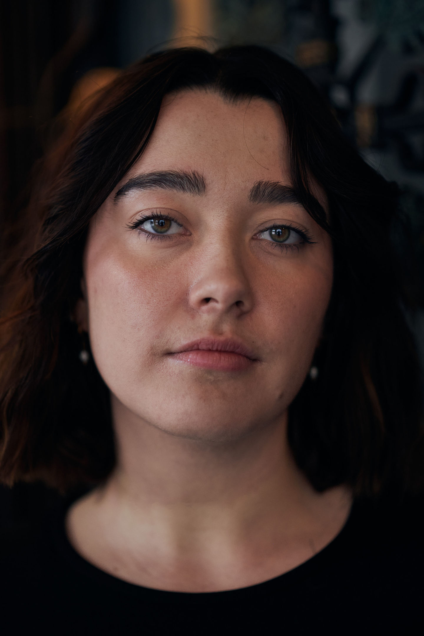 Headshot einer jungen Schauspielerin mit braunen Haaren und grünen Augen, die herausfordernd in die Kamera blickt